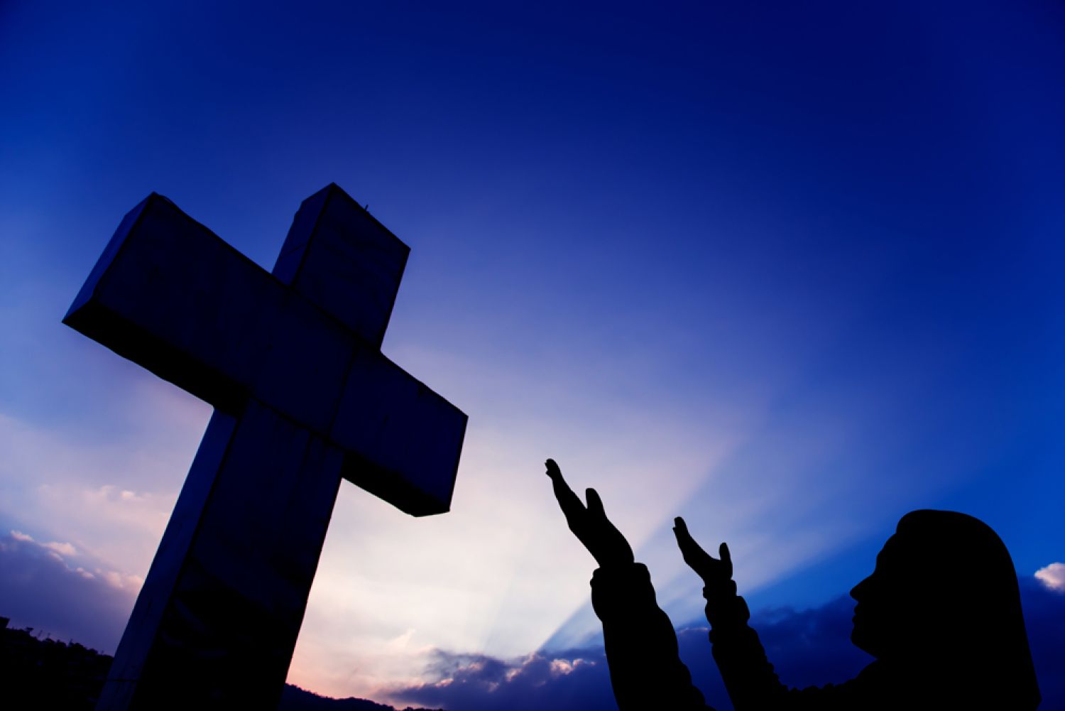 Kreuz vor Abendhimmel und betendem Menschen
